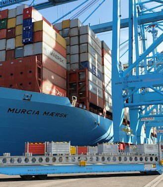 A sleek cargo ship docked at a bustling port with containers labeled electronics and industrial equipment.
