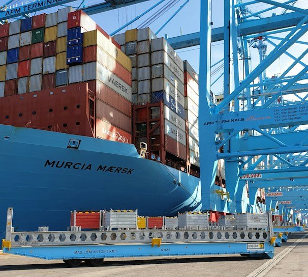 A sleek cargo ship docked at a bustling port with containers labeled electronics and industrial equipment.
